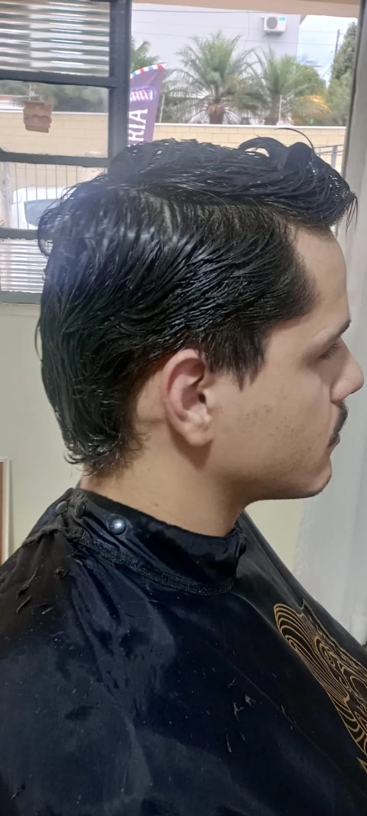 Corte masculino com topo penteado para trás e laterais baixas, visto de perfil